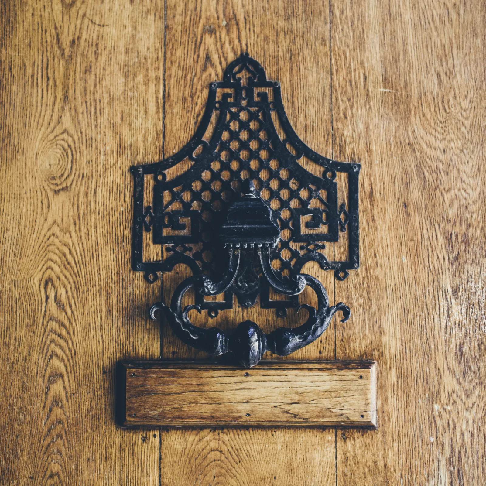 Black ornamental metal wall sconce with a decorative latticed canopy and a curved bracket, mounted on wood paneling at Hôtel Villas Foch in Bordeaux
