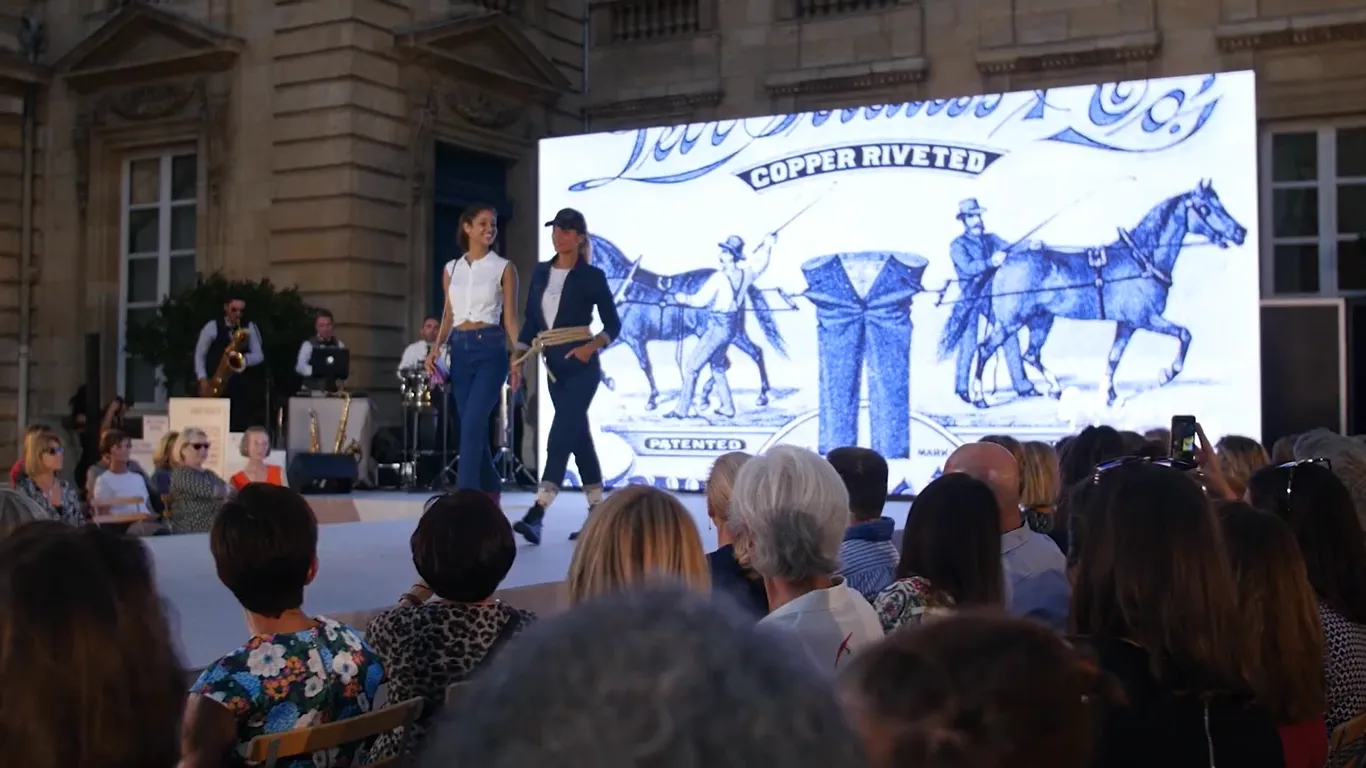 Fashion show event in Bordeaux featuring models on a runway with a large screen displaying Copper River branding and Western-themed illustrations, with live musicians and an audience watching the presentation.