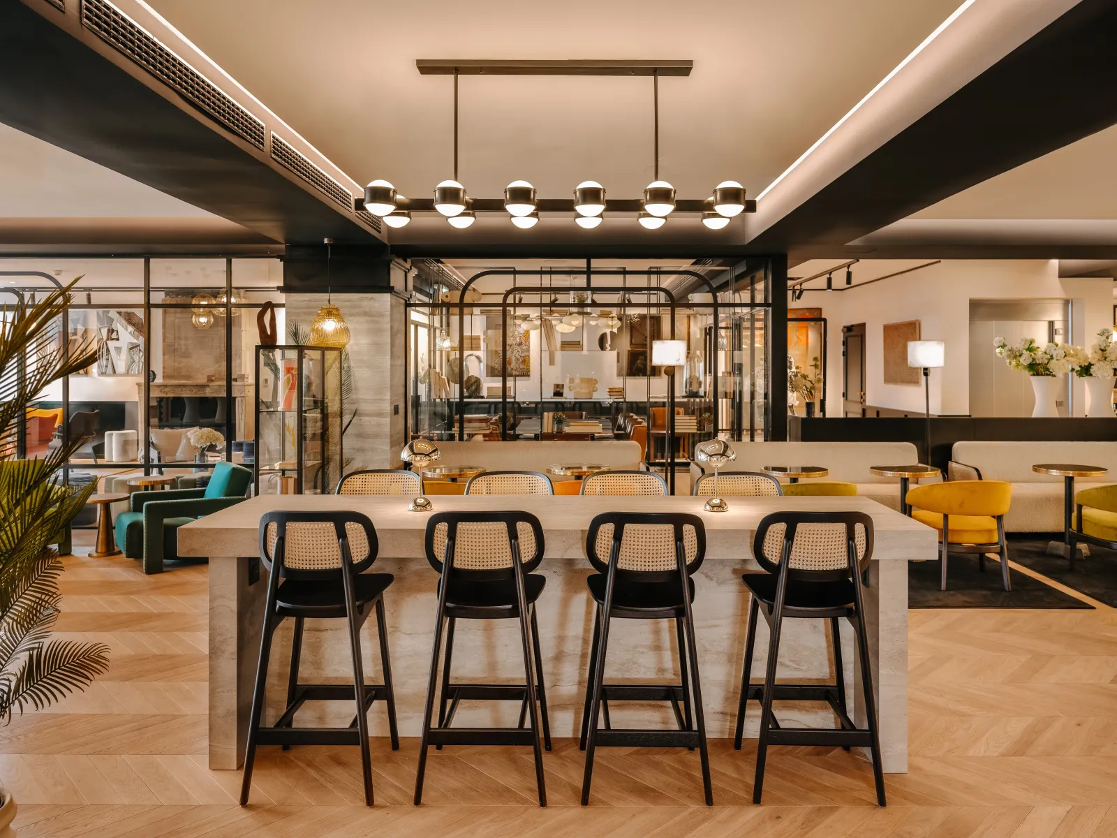 Modern hotel lounge at Marty Hotel Bordeaux featuring a contemporary bar counter with black rattan bar stools, wooden flooring, and ambient lighting under a coffered ceiling with decorative pendant lights.
