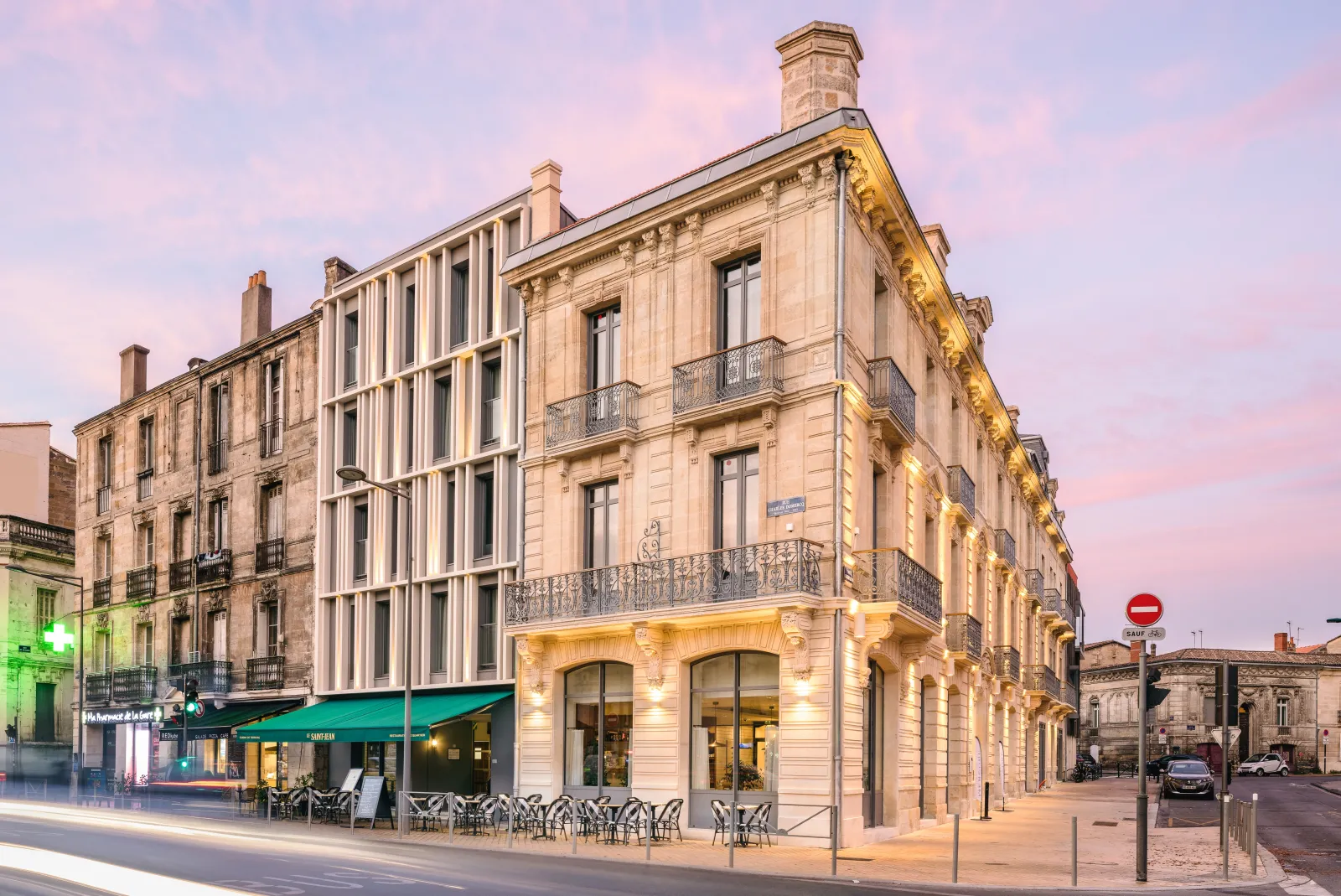 Mercure Bordeaux Gare Atlantic hotel, a beige stone building with classical architecture, ground floor retail spaces with green awning, and ornate wrought iron balconies, photographed at twilight in Bordeaux.