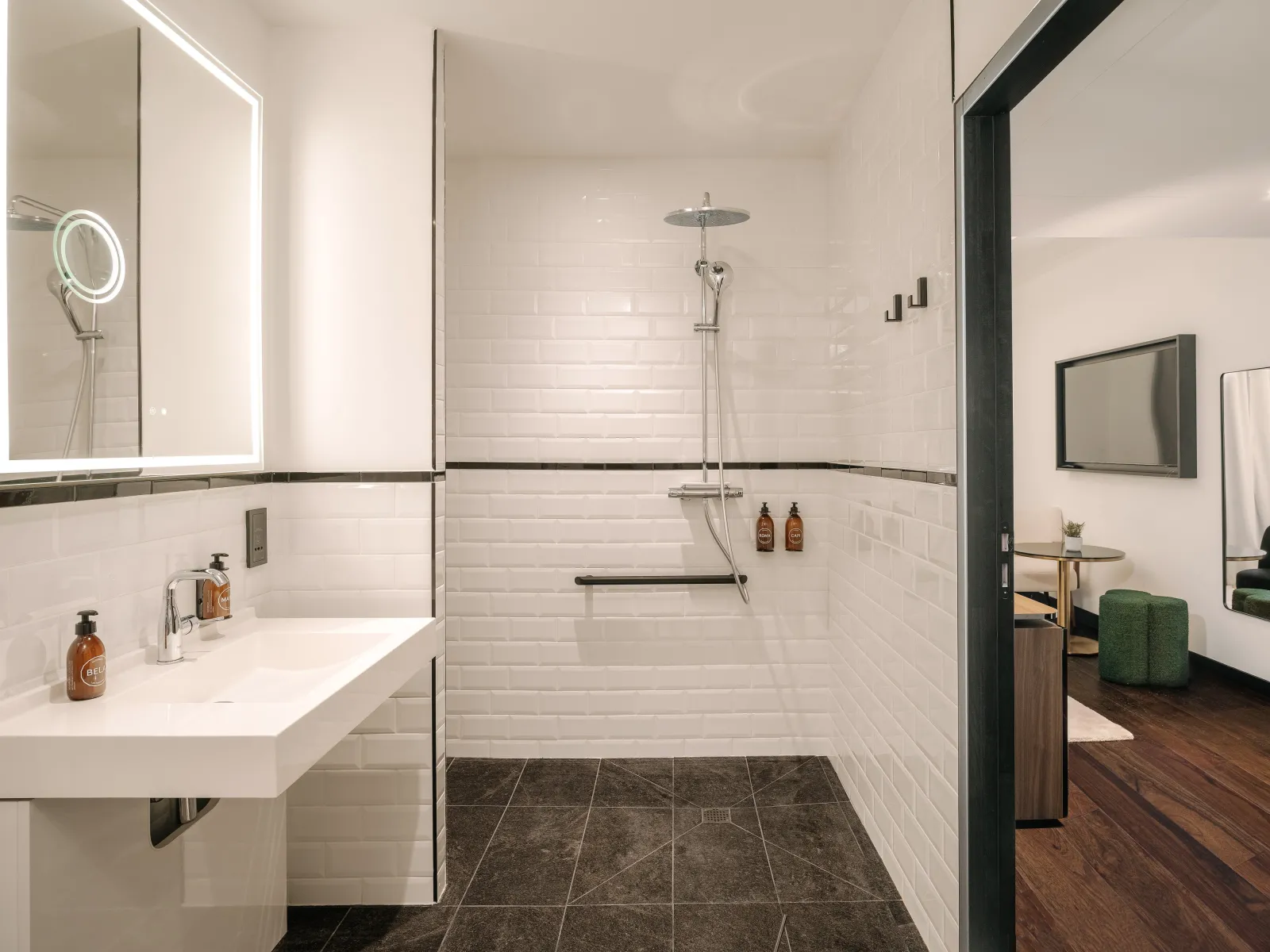 Modern bathroom at Marty Hotel Bordeaux featuring a walk-in shower with white subway tiles, floating vanity with illuminated mirror, dark tile flooring, and contemporary fixtures with black metal accents.