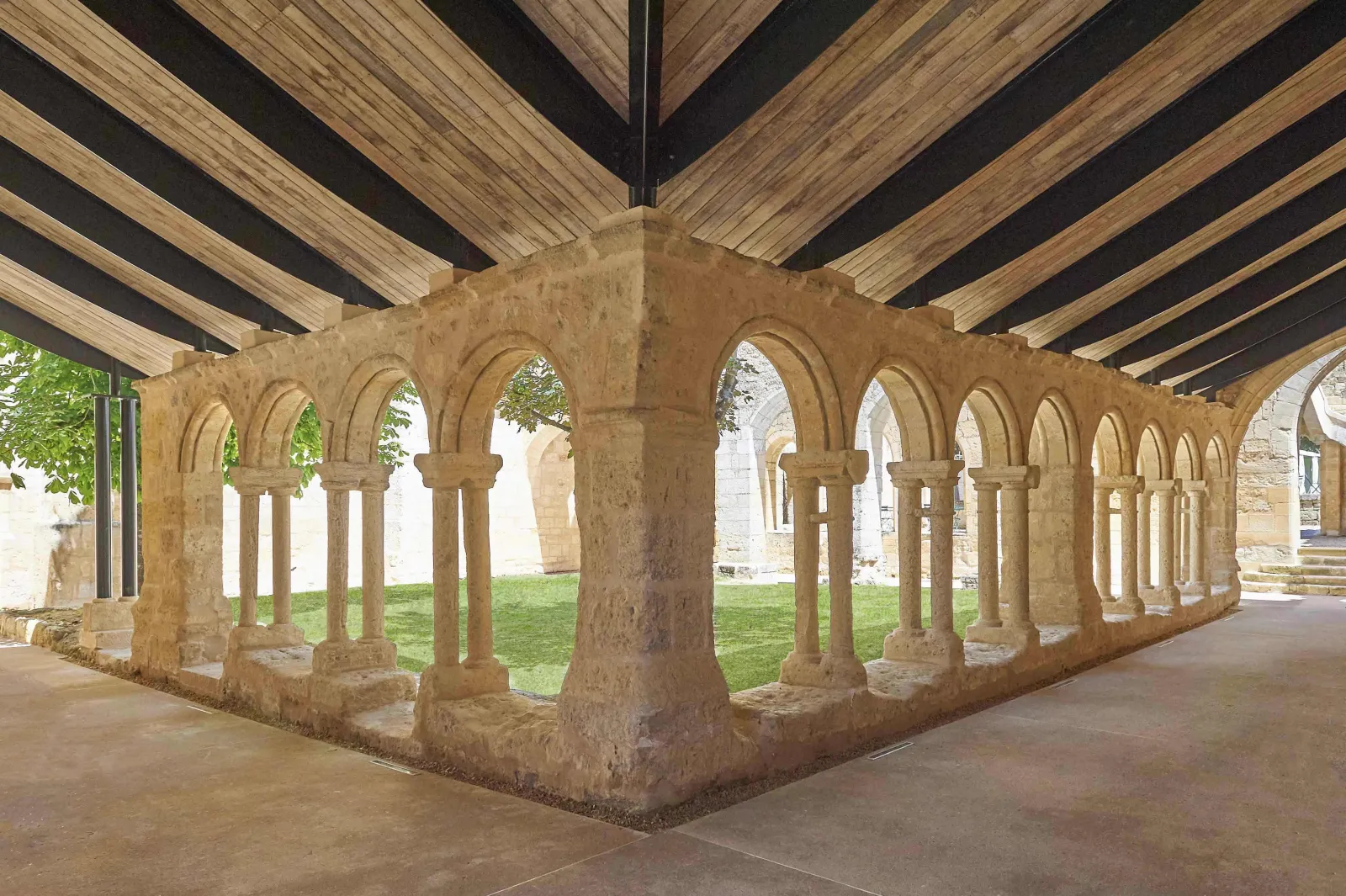 Medieval stone cloister with Romanesque arches and columns beneath wooden ceiling beams, part of the Cordeliers monastery in Bordeaux
