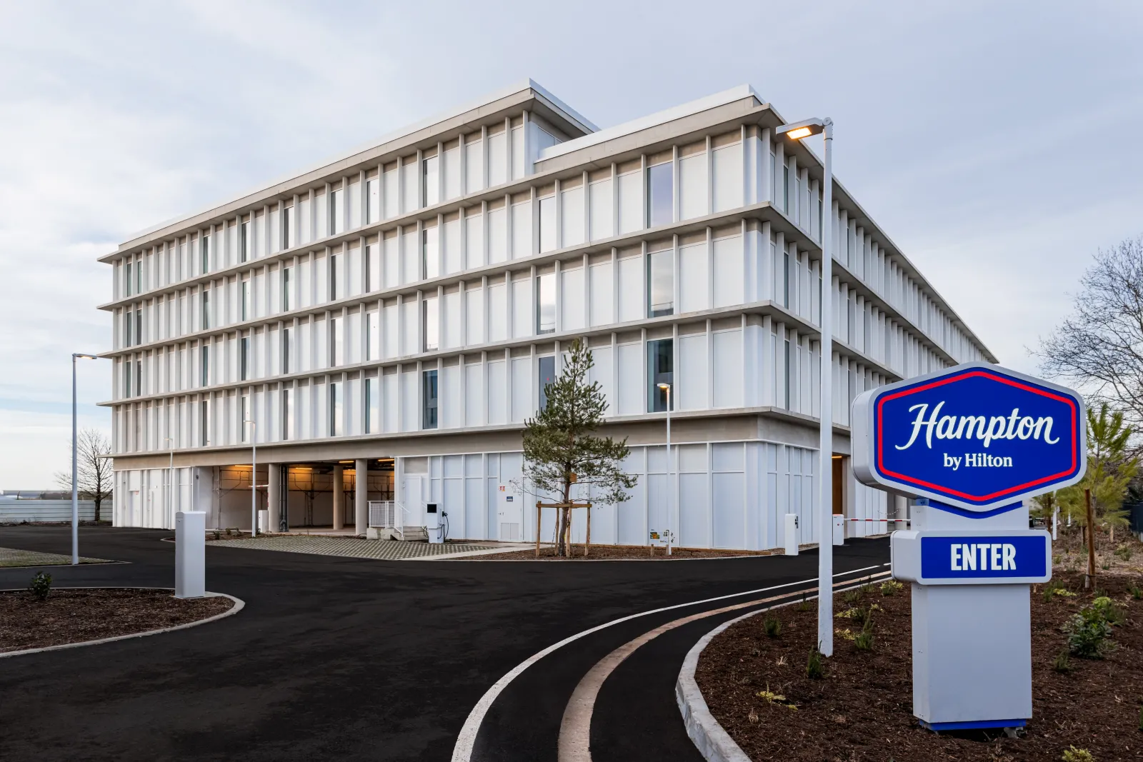 Modern Hampton by Hilton hotel building with white vertical striped facade and glass windows, featuring entrance sign in Bordeaux Mérignac