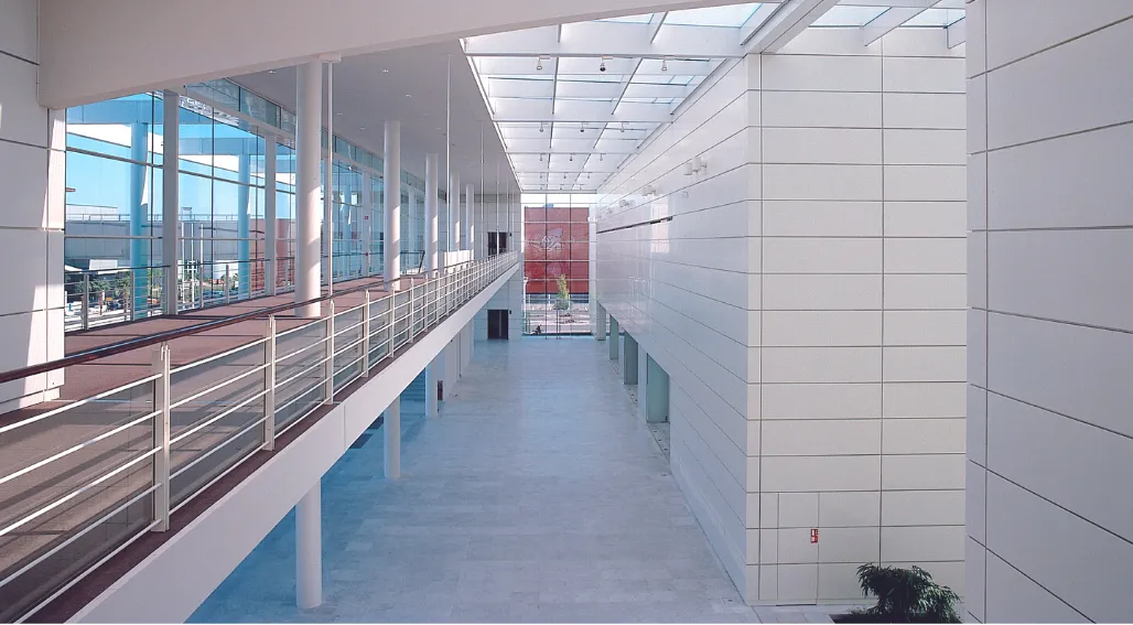 Interior corridor of Bordeaux Congress Centre with modern white tile walls, skylight ceiling, metal railings, and large windows overlooking the city skyline