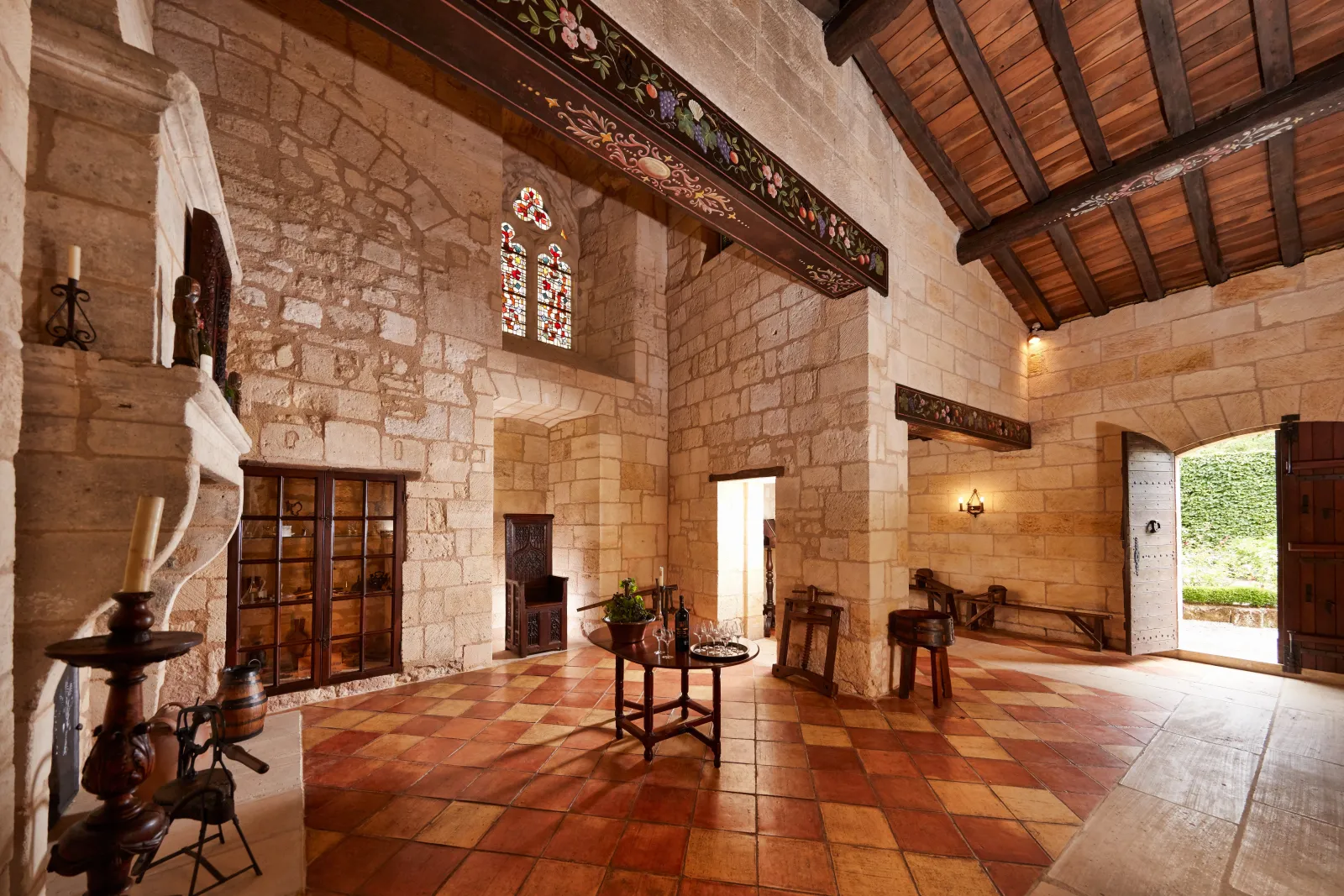 Interior of the Jacobins Convent in Bordeaux, showing a vast stone hall with terracotta tile flooring, wooden ceiling beams, stained glass windows, and antique furniture