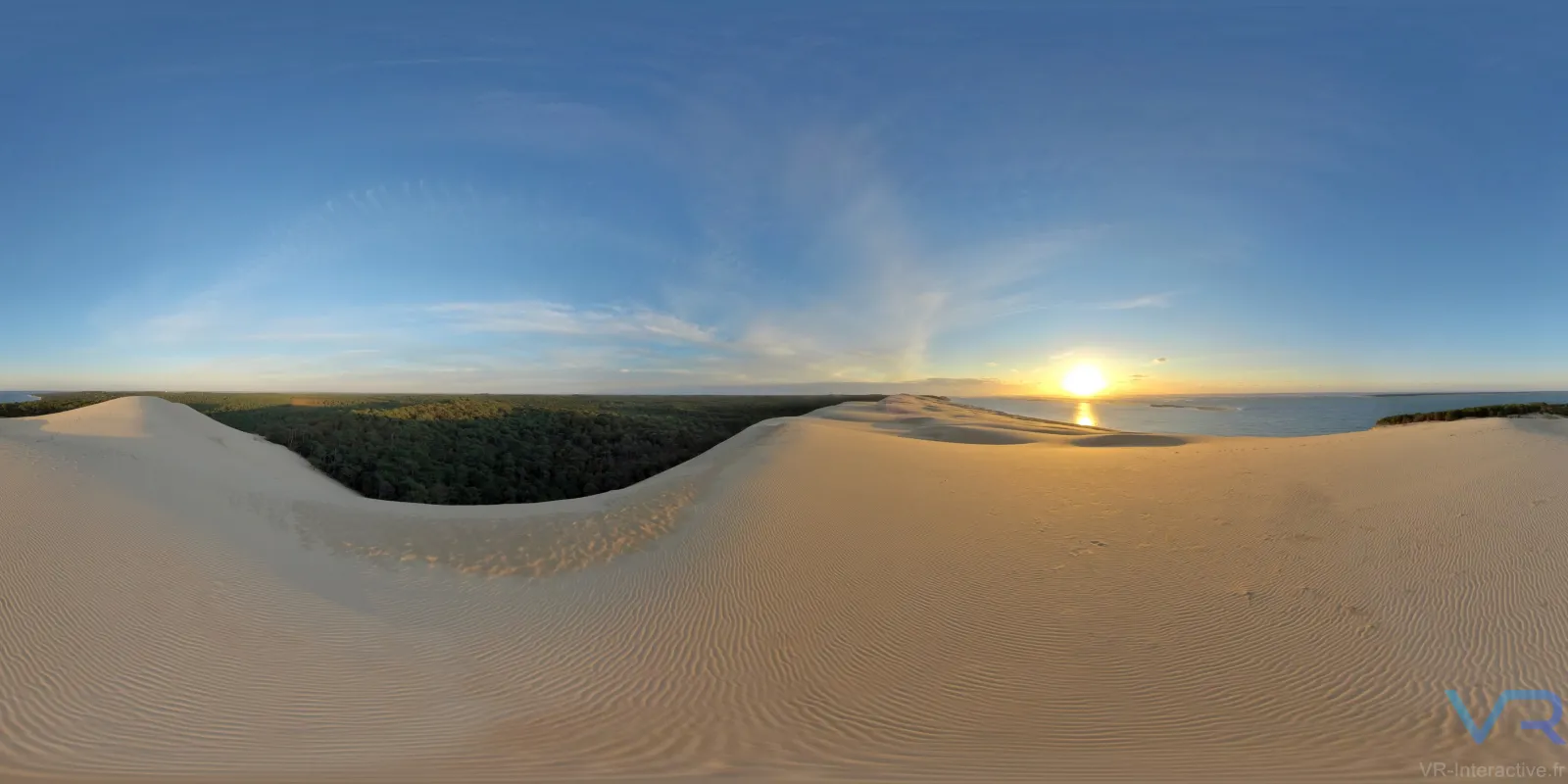 Panoramic view of the Dune du Pilat at sunset, showing vast sand dunes with rippled texture, a forested valley in the center, and the Atlantic Ocean on the horizon under a golden sky.