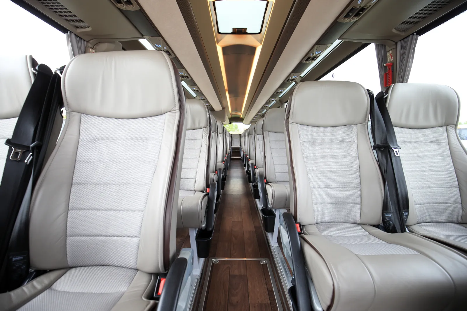 Interior view of a modern coach bus with light gray upholstered seats, wooden floor, and ambient lighting running down the center aisle