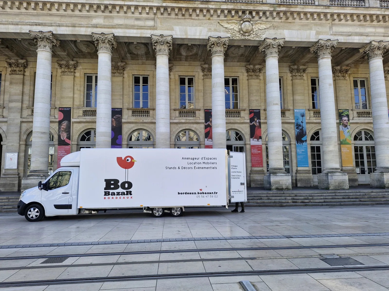 White mobile promotional truck for Bo Bazar parked in front of a classical building with Corinthian columns in Bordeaux, displaying service information for event spaces and furniture rental.