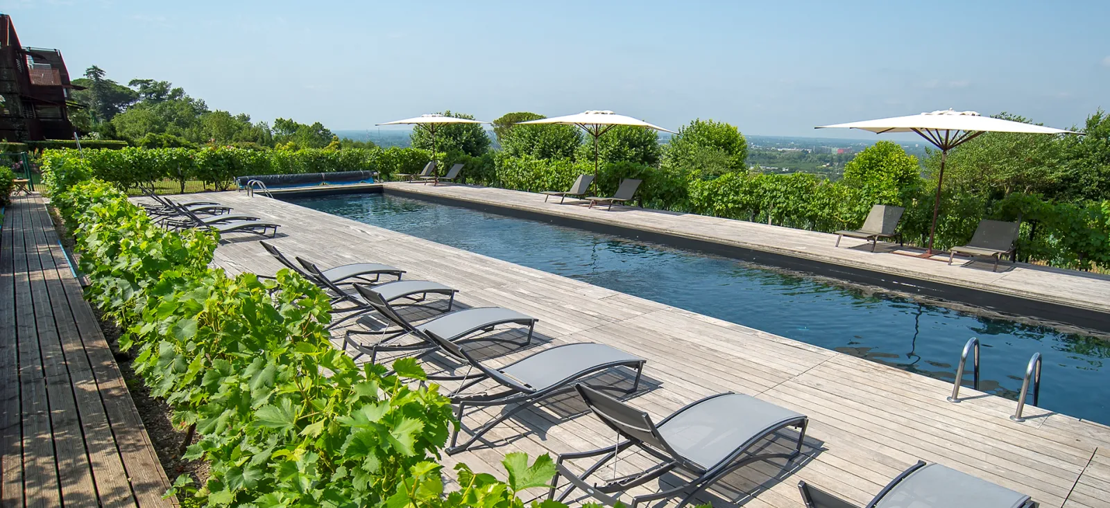 Luxury infinity pool with loungers and white umbrellas overlooking vineyards and the countryside at Le Saint-James hotel in Bordeaux