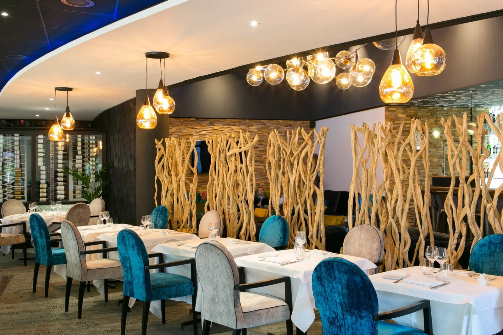 Modern restaurant dining room at Mercure Bordeaux Airport hotel with elegant white tablecloths, blue velvet chairs, decorative golden branch panels, and warm pendant lighting