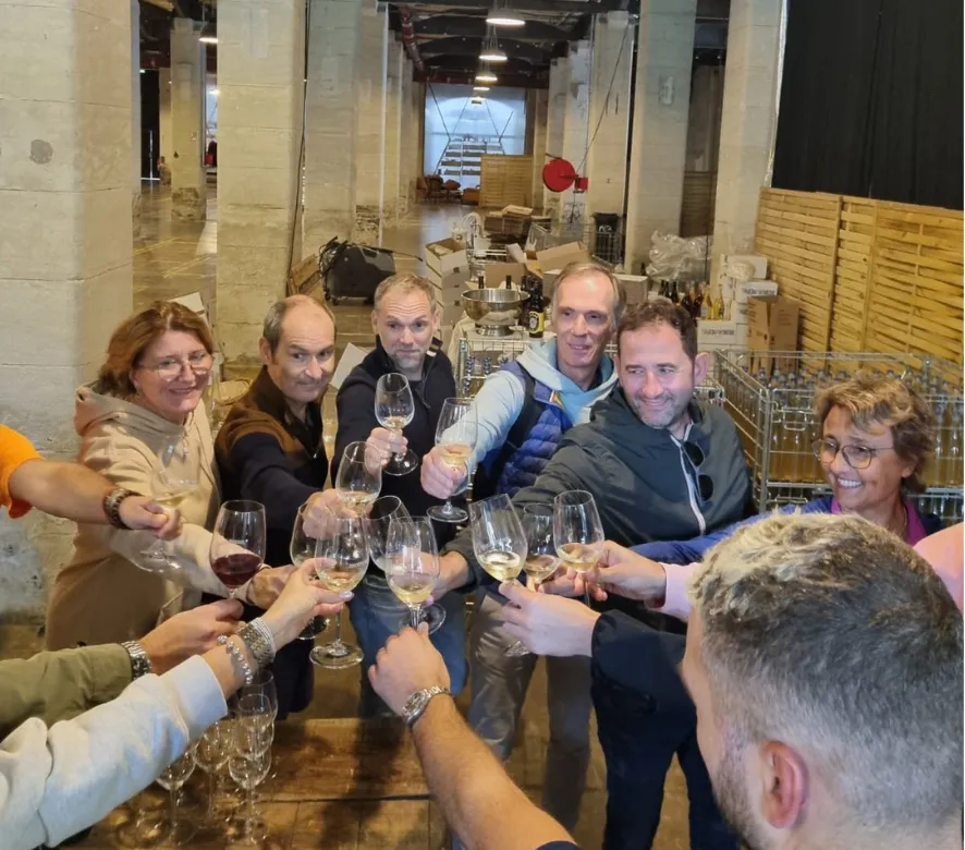 A group of people toasting with wine glasses in an industrial warehouse setting, celebrating together during a wine tasting event in Bordeaux.