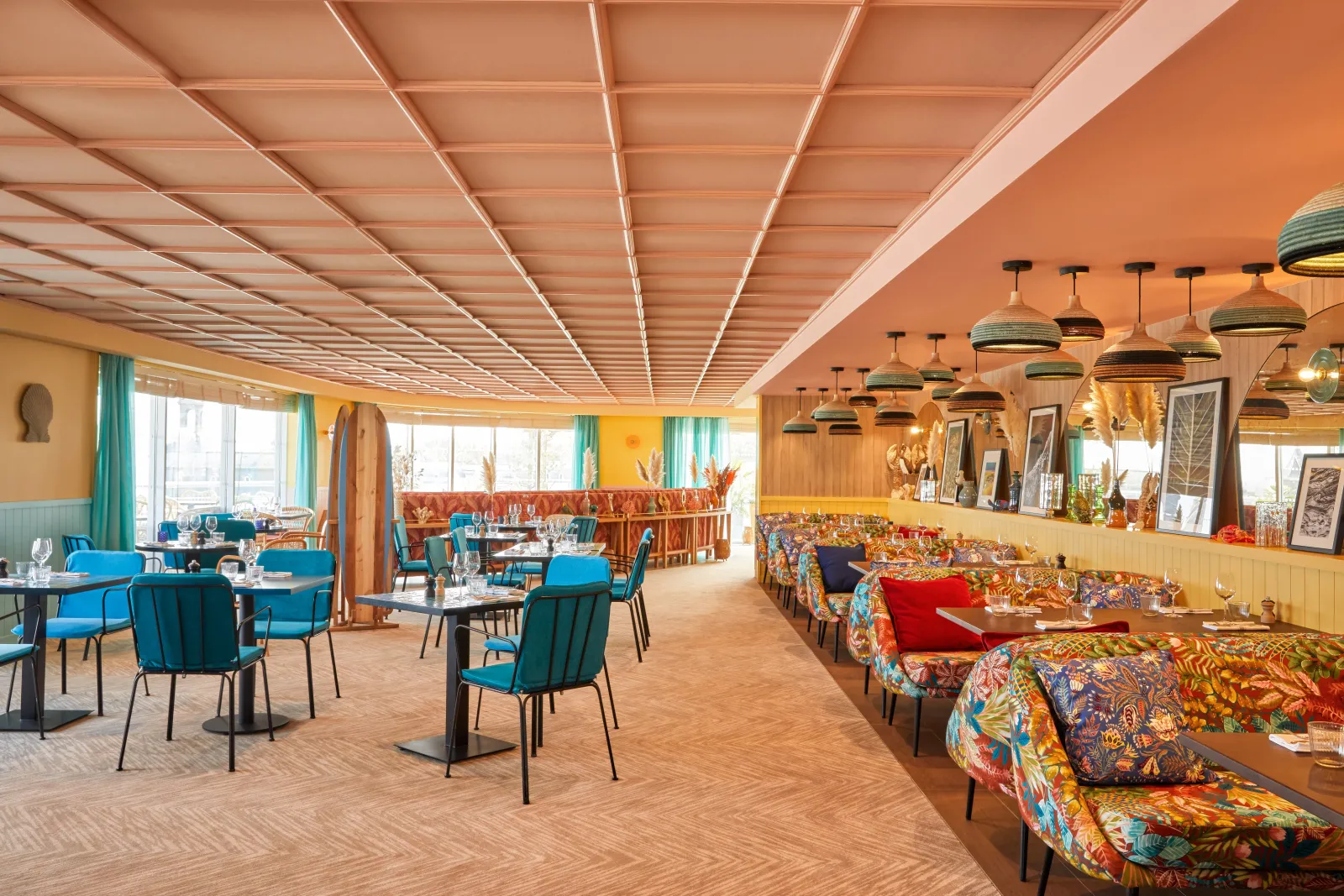 Modern hotel restaurant and lounge area with colorful banquette seating, blue chairs, geometric ceiling design, pendant lighting, and large windows overlooking Bordeaux