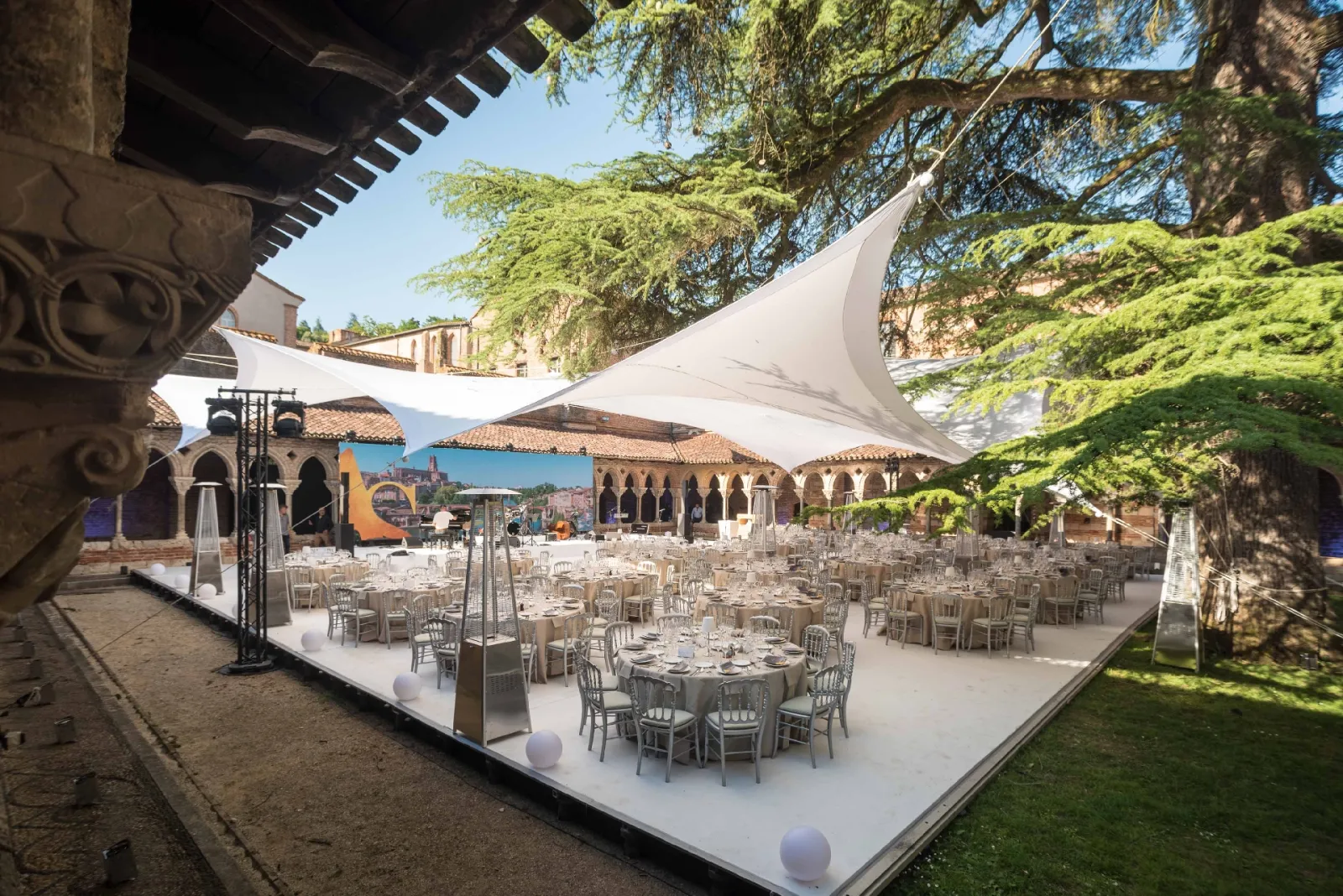 Elegant outdoor wedding reception setup in a historic courtyard with round tables, white chairs, and large white tent canopies, surrounded by Renaissance architecture and lush ivy-covered walls.
