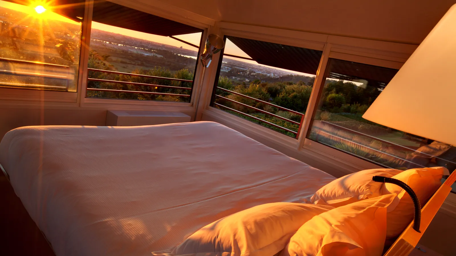 Sunrise view from a modern bedroom with floor-to-ceiling windows overlooking the Bordeaux valley and vineyards, featuring a bed with yellow bedding and contemporary furnishings