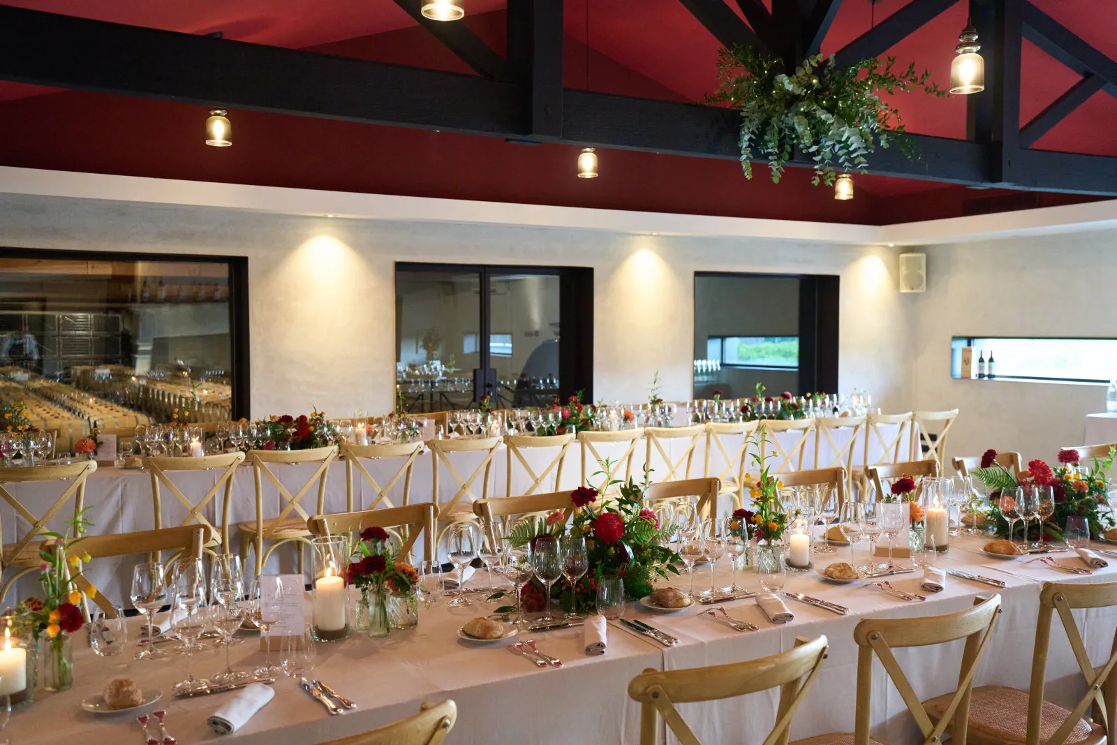 Elegant banquet hall at Château Marquis de Terme in Bordeaux with long dining tables set for a formal event, featuring white linens, wooden cross-back chairs, floral centerpieces with red roses, candles, and a striking red ceiling with black beams.