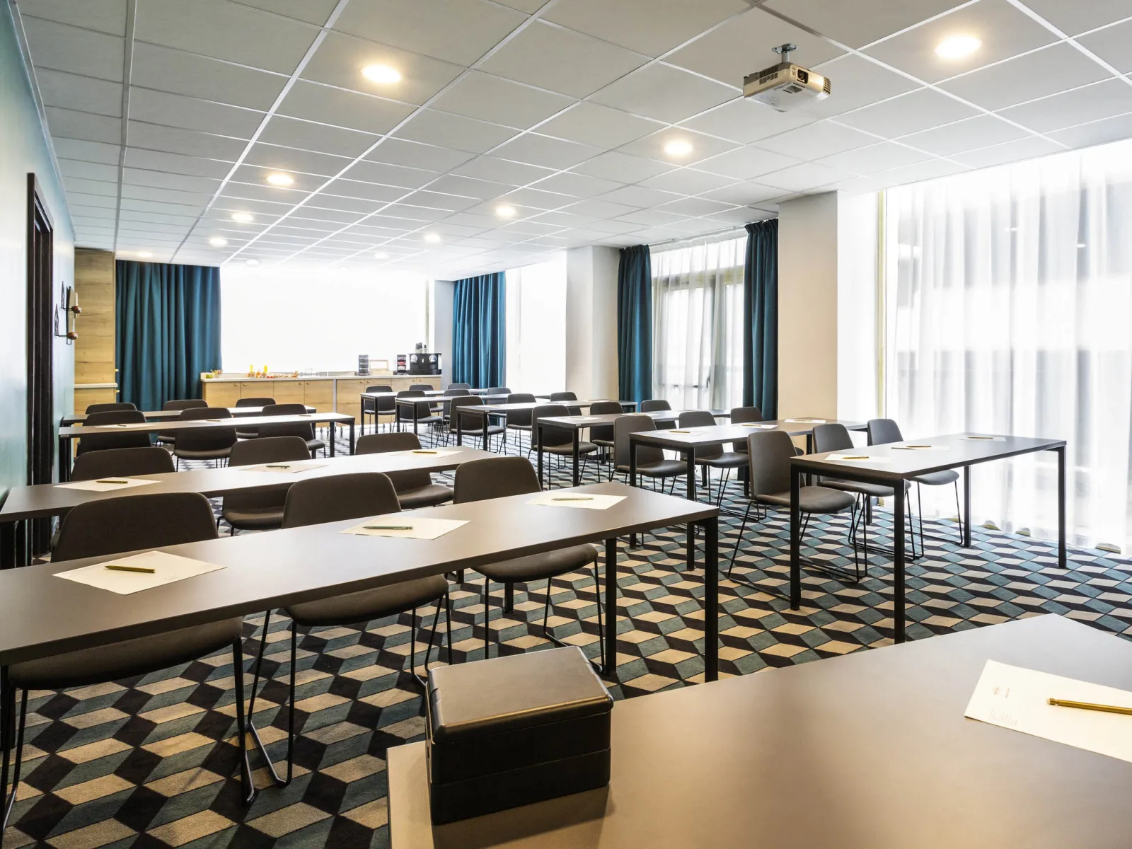 Modern conference room at Mercure Bordeaux Centre hotel with multiple white tables, black chairs, geometric patterned carpet, blue curtains, large windows with city views, and recessed ceiling lights