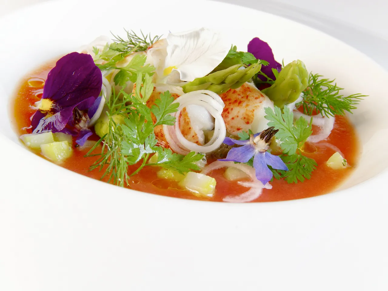 Gourmet seafood dish with shrimp, fresh herbs, edible flowers, and red sauce on a white plate