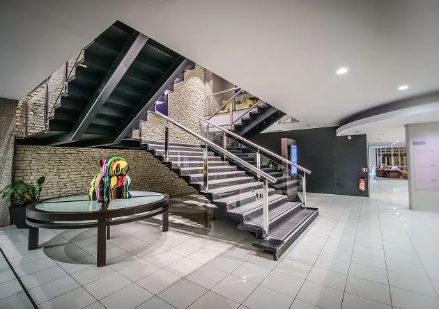 Modern hotel lobby with a grand staircase, tiled flooring, brick wall, colorful parrot sculpture on a round table, and contemporary lighting at Pullman Bordeaux Lac.