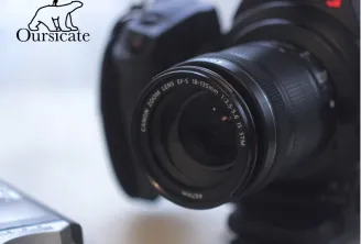 Close-up of a Canon EOS camera with an 18-135mm zoom lens, displayed with photography equipment in a professional studio setting