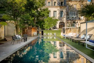 Luxury courtyard with a rectangular reflecting pool, lined with lounge chairs and sun beds, surrounded by manicured gardens and a historic Haussmann-style mansion in Bordeaux