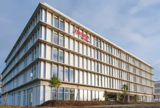 Modern Hampton by Hilton hotel building in Bordeaux Mérignac with contemporary architecture featuring white vertical louvers, multiple floors with large windows, and landscaped entrance.