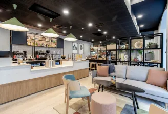 Modern aparthotel lounge and café area with white counter, wooden accents, comfortable seating, shelving displays, and contemporary lighting at Staycity Bordeaux City Centre