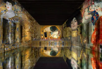 Immersive digital art installation at Bassins des Lumières in Bordeaux, featuring large-scale projections of Gustav Klimt's portraits and masterpieces on warehouse walls, with reflections on water floor.