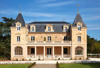 Château Léognan, a 19th-century neoclassical mansion in Bordeaux featuring two symmetrical towers with pointed roofs, cream-colored stone façade, ornate balustrades, and a covered colonnade entrance, set in manicured gardens.