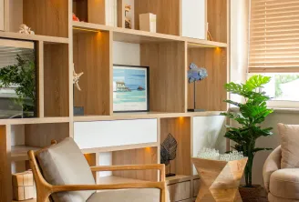 Modern living room with wooden modular shelving unit, mid-century armchair, potted plants, decorative accessories, and beach-themed artwork in a contemporary interior.