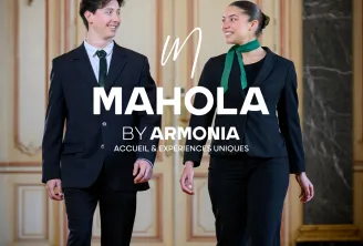 Two professionally dressed staff members walking through an elegant classical corridor with ornate cream and gold paneling, promoting Mahola by Armonia hospitality services in Bordeaux.
