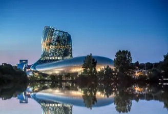 Night view of the Cité du Vin museum in Bordeaux, an illuminated modern building with curved glass and steel architecture reflected in the adjacent river.