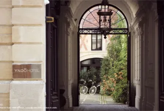 Entrance to Yndo Hotel in Bordeaux showing an elegant arched doorway with wrought iron details, leading to a courtyard with ivy-covered walls and bicycles