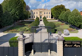 Grand entrance gate of the Bernard Magrez Cultural Institute in Bordeaux, with a neoclassical mansion visible beyond manicured gardens and topiary hedges.