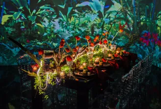 Elegant table setting with red flowers, candles, and greenery under a vibrant botanical projection backdrop