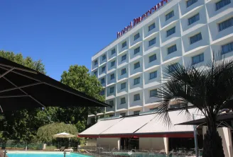 Mercure hotel building with white facade overlooking a swimming pool with red and white umbrellas and palm trees under blue sky in Bordeaux-Lac