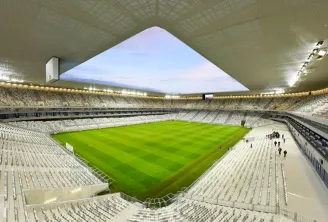 Interior view of Stade Atlantique Bordeaux Métropole, a modern football stadium with white seating, a bright green pitch, and a distinctive angular roof opening to the sky.