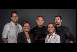 Five smiling team members from Maison Dulou Traiteur posing together against a gray background, with the company logo visible on one person's shirt