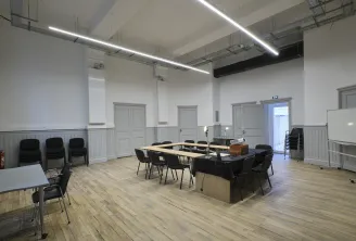 Modern conference room at ManuCo in Bordeaux featuring a large wooden table with black chairs, white walls with wainscoting, linear ceiling lights, and multiple doors leading to other spaces.