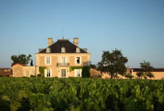 Château Haut-Bailly, a classical French mansion with mansard roof and cream-colored stone facade, surrounded by vineyard rows in Bordeaux wine region