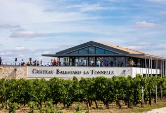 Modern winery building of Château Balestard La Tonnelle with vineyard in foreground, located in Bordeaux wine region, featuring contemporary architecture with large windows and visitors on the terrace