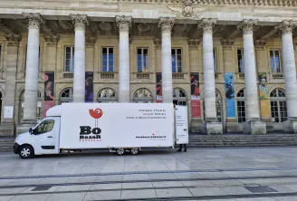 White mobile promotional truck for Bo Bazar parked in front of a classical building with Corinthian columns in Bordeaux, displaying service information for event spaces and furniture rental.