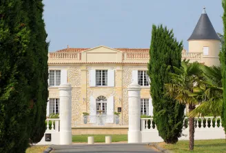 Château Lafitte in Bordeaux, France: A neoclassical mansion with cream and stone facade, white columns, mansard roof with dormer windows, round tower with conical roof, flanked by tall cypress trees and palm trees, featuring manicured gardens and balustra
