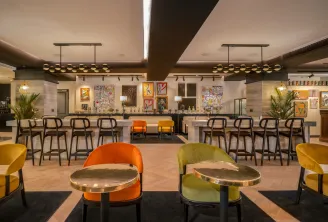 Modern hotel bar and lounge area at Marty Hôtel Bordeaux featuring colorful upholstered chairs, brass-topped tables, dual bar counters with pendant lighting, and contemporary artwork on the walls.
