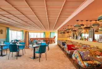 Modern hotel restaurant and lounge area with colorful banquette seating, blue chairs, geometric ceiling design, pendant lighting, and large windows overlooking Bordeaux