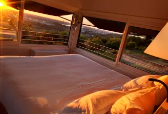 Sunrise view from a modern bedroom with floor-to-ceiling windows overlooking the Bordeaux valley and vineyards, featuring a bed with yellow bedding and contemporary furnishings