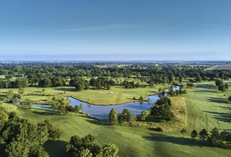 Aerial view of Bordeaux Lac Golf course featuring manicured greens, scattered trees, and a winding blue water hazard under clear skies