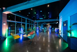 Modern lounge space at Cap Sciences Bordeaux with colorful neon lighting, contemporary seating areas, floor-to-ceiling windows overlooking the city, and green plant accents throughout.