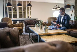 Professional man in business attire working at a wooden table in a modern lounge area with leather armchairs, pendant lights, and contemporary decor at Pullman Bordeaux Lac hotel
