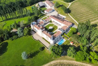 Aerial view of Château Toulouse-Lautrec near Bordeaux, showing a white stone castle with terracotta roofs, swimming pool, manicured grounds, surrounding vineyards and farmland, nestled among green vegetation and trees.