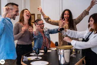 A group of five people laughing and celebrating around a dining table with wine glasses and place settings during an Invino wine event in Bordeaux.